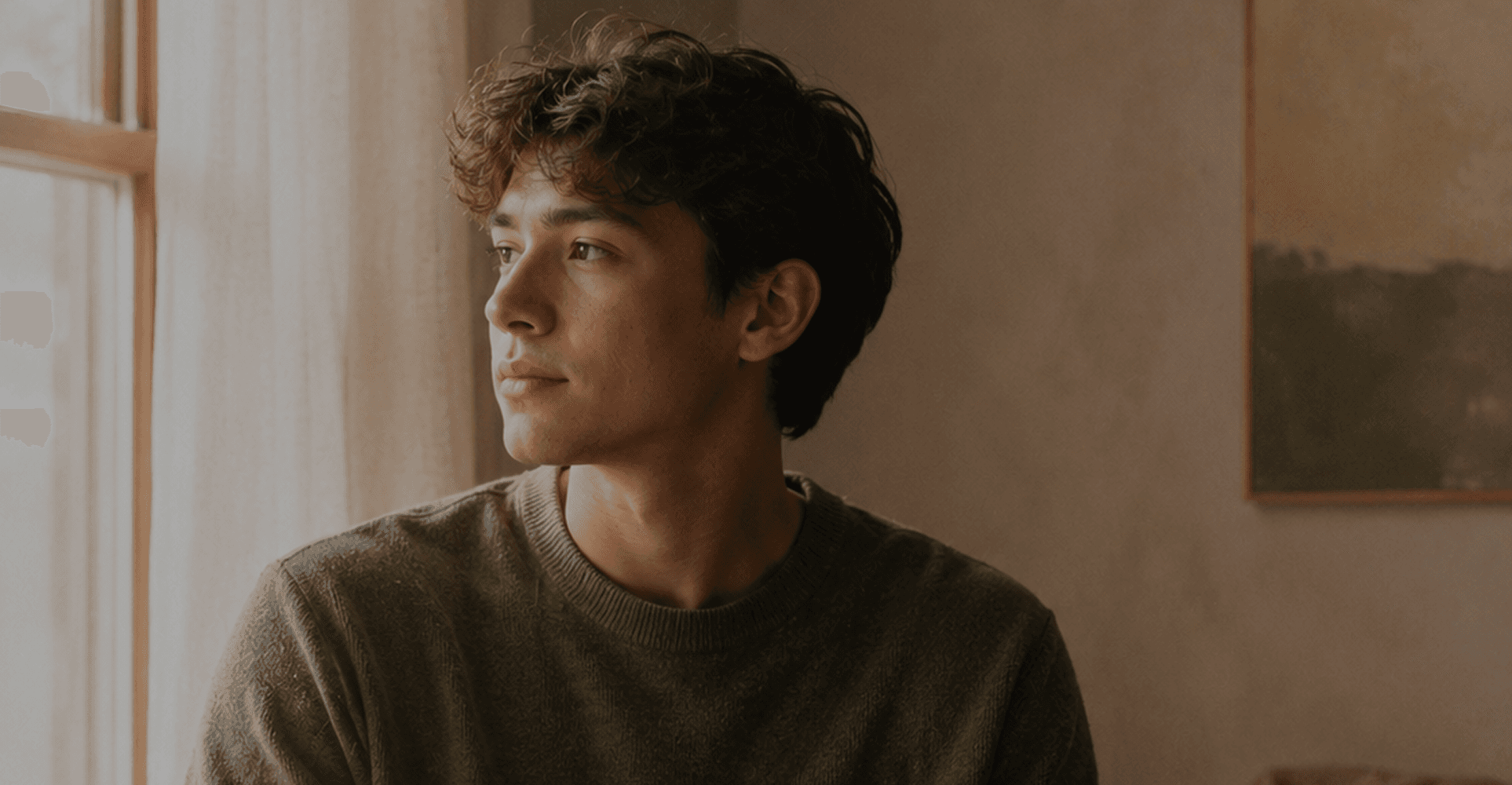A young man looking out a sunlit window