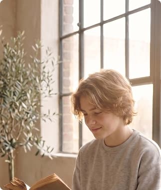 A teenager reading quietly by a sunlit window
